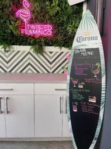 Corona surfboard chalkboard sign with a handwritten drink menu at an outdoor tiki bar