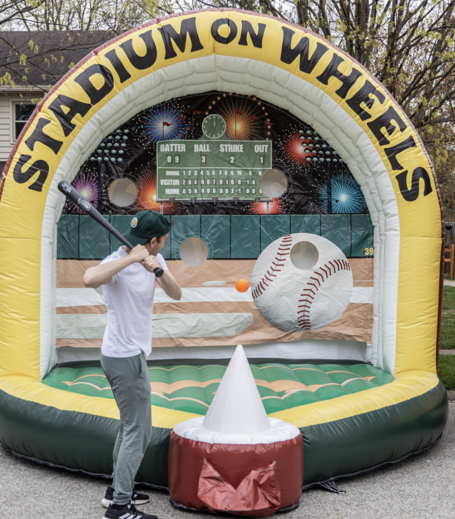 Person swinging a baseball bat inside a large branded inflatable baseball batting cage outdoors.