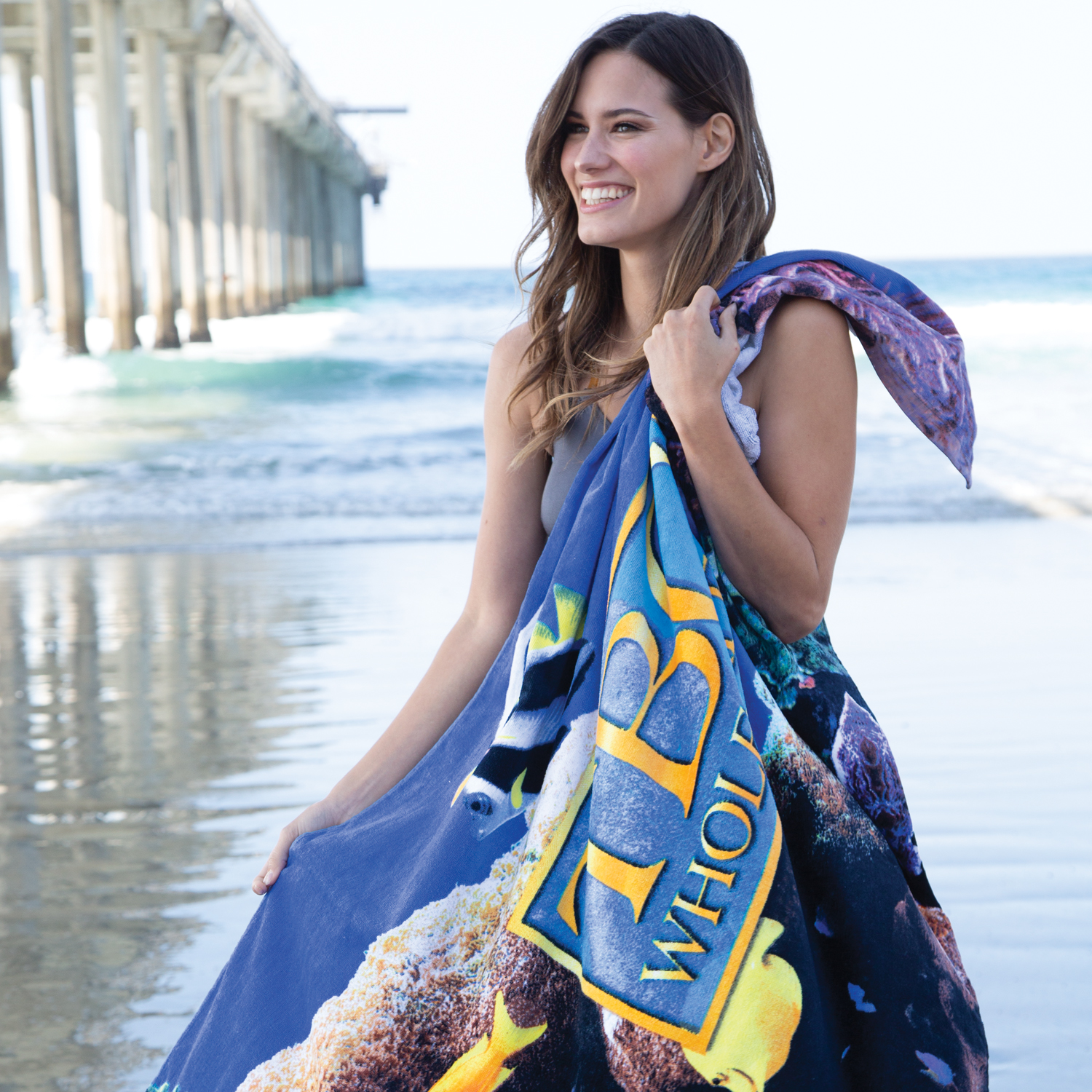 Colorful custom branded beach towel with bold logo worn at beach by woman in swimwear
