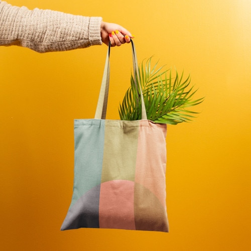Hand holding custom pigment-dyed canvas tote with full-color edge-to-edge branded print design
