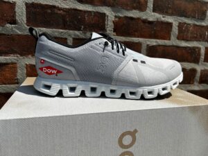 Light gray On running shoe with a small red custom logo on the side near the heel