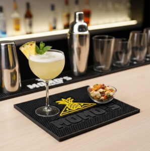 Custom molded PVC bar mat with a raised logo under a cocktail on a busy back bar